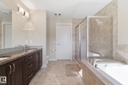 Bathroom featuring a double vanity with granite countertops, a tiled shower with a glass enclosure, a white built-in bathtub, and tiled flooring - 