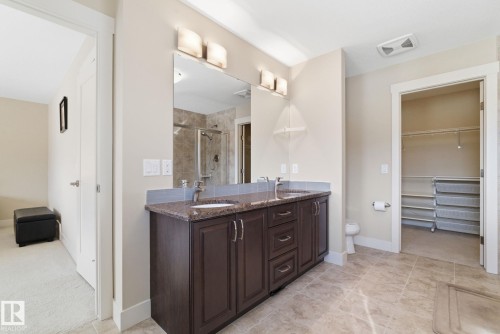 This bathroom features a double vanity with a granite countertop, a large mirror with sconce lighting, and tiled flooring - 3235 Abbott Crescent, Edmonton, AB - Indoor Photo Showing Bathroom
