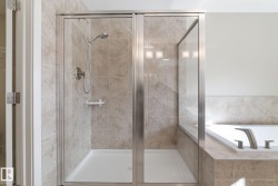 The bathroom features a tiled shower with a glass enclosure and a white bathtub with brushed nickel fixtures - 