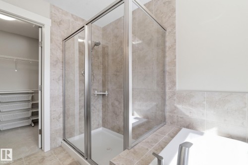 Bathroom featuring a glass-enclosed shower, tiled walls and flooring, and a portion of a white bathtub - 3235 Abbott Crescent, Edmonton, AB - Indoor Photo Showing Bathroom