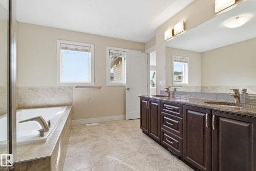 Bathroom featuring a built-in bathtub with tiled surround, a double vanity with dark wood cabinetry and granite countertops, and tiled flooring - 3235 Abbott Crescent, Edmonton, AB - Indoor Photo Showing Bathroom