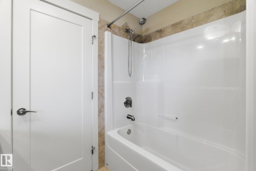 Bathroom featuring a white bathtub and shower combination with a handheld showerhead and wall-mounted faucet, complemented by tiled walls - 3235 Abbott Crescent, Edmonton, AB - Indoor Photo Showing Bathroom