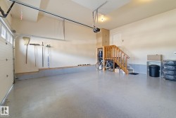 This garage features an automatic overhead door, light-colored walls, and a staircase with wooden handrails - 