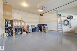 Spacious garage featuring a concrete floor, light-colored walls, and a wooden staircase - 
