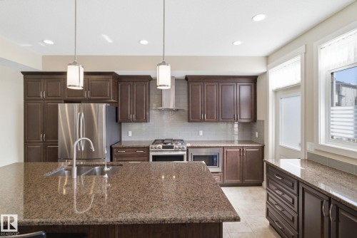 The kitchen features dark wood cabinetry, stainless steel appliances, and granite countertops - 3235 Abbott Crescent, Edmonton, AB - Indoor Photo Showing Kitchen With Double Sink With Upgraded Kitchen