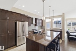 The kitchen features dark wood cabinetry, stainless steel appliances, a large island with a granite countertop, and pendant lighting - 