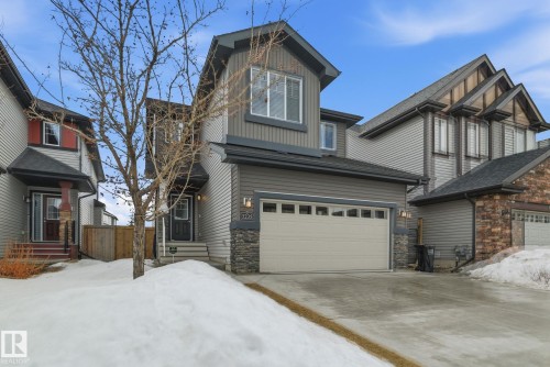 The property features a two-story design with gray siding and stone accents on the facade, a two-car garage with a light-colored door, and a paved driveway - 3235 Abbott Crescent, Edmonton, AB - Outdoor With Facade