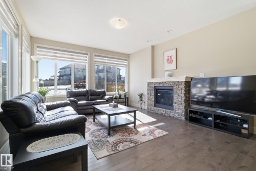 Living room featuring hardwood-style flooring, a stone-faced fireplace with a mantel, and large windows with blinds providing natural light - 3235 Abbott Crescent, Edmonton, AB - Indoor Photo Showing Living Room With Fireplace