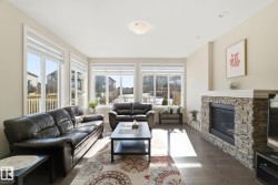 Living room featuring hardwood style flooring, a stone-clad fireplace with a white mantel, and large windows providing natural light - 