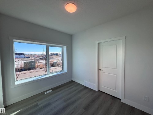 The room features a window providing views of the surrounding area, a ceiling light fixture, a white paneled door, and grey wood-look flooring - 2740 Blatchford Road, Edmonton, AB - Indoor Photo Showing Other Room