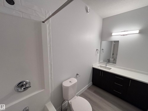 Bathroom featuring a white bathtub with subway tile surround, a dark wood vanity with a white countertop, and a rectangular mirror with an overhead light fixture - 2740 Blatchford Road, Edmonton, AB - Indoor Photo Showing Bathroom