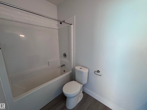 Bathroom featuring a white bathtub with a shower and a toilet, set against light-colored walls and wood-look flooring - 2740 Blatchford Road, Edmonton, AB - Indoor Photo Showing Bathroom