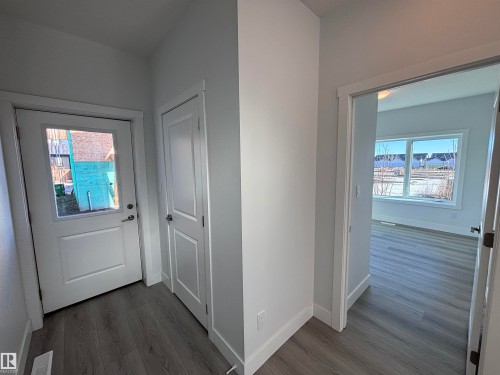 The property features a bright entryway with durable plank flooring, a white door with a window, and a white interior door, leading into a room with large windows - 2740 Blatchford Road, Edmonton, AB - Indoor Photo Showing Other Room
