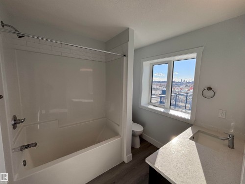 The bathroom features a combination tub and shower with subway tile surround, a window providing natural light and city views, and a vanity with a countertop and undermount sink - 2740 Blatchford Road, Edmonton, AB - Indoor Photo Showing Bathroom