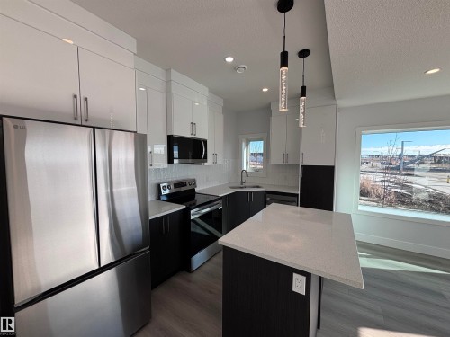 The kitchen features stainless steel appliances, a center island with a light-colored countertop, dark lower cabinetry, and white upper cabinetry - 2740 Blatchford Road, Edmonton, AB - Indoor Photo Showing Kitchen With Upgraded Kitchen