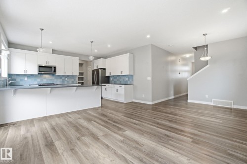 The kitchen features white cabinetry, stainless steel appliances, a light blue tiled backsplash, and recessed lighting - 1607 202 Street, Edmonton, AB - Indoor Photo Showing Kitchen With Upgraded Kitchen