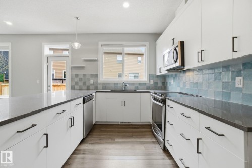 Well-appointed kitchen featuring white cabinetry, dark countertops, a blue tiled backsplash, stainless steel appliances, and wood-style flooring - 1607 202 Street, Edmonton, AB - Indoor Photo Showing Kitchen With Upgraded Kitchen