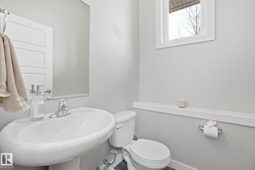 This bathroom features a pedestal sink with a chrome faucet, a wall-mounted mirror, and a toilet - 1607 202 Street, Edmonton, AB - Indoor Photo Showing Bathroom