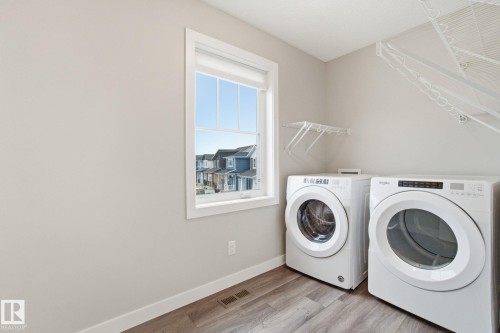 Laundry area featuring a window, light-colored walls, white appliances, and wood-look flooring - 1607 202 Street, Edmonton, AB - Indoor Photo Showing Laundry Room