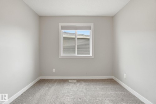 This room features light grey walls, a white framed window, and grey carpet flooring - 1607 202 Street, Edmonton, AB - Indoor Photo Showing Other Room