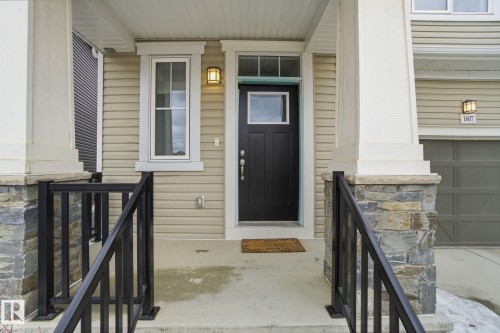 The property features an inviting entrance with a dark colored front door, complemented by a window and exterior lighting - 1607 202 Street, Edmonton, AB - Outdoor With Exterior