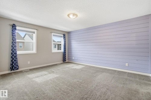 Spacious room featuring light grey carpet, two windows providing natural light, and a decorative accent wall with horizontal paneling - 1607 202 Street, Edmonton, AB -  Photo Showing Other Room