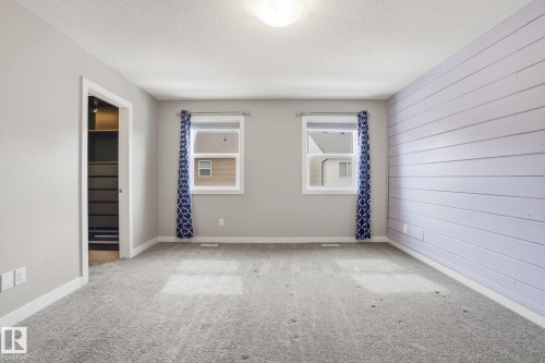Spacious room featuring light grey walls, a textured accent wall, two windows, and grey carpeting - 1607 202 Street, Edmonton, AB - Indoor Photo Showing Other Room
