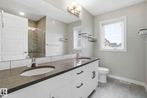 The bathroom features a dual sink vanity with a dark countertop and white cabinetry, a large mirror, a window providing natural light, and tiled flooring - 1607 202 Street, Edmonton, AB - Indoor Photo Showing Bathroom