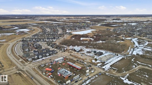 Aerial view showcasing a residential area with a curved road, surrounded by undeveloped land and a body of water - 1607 202 Street, Edmonton, AB - Outdoor With View
