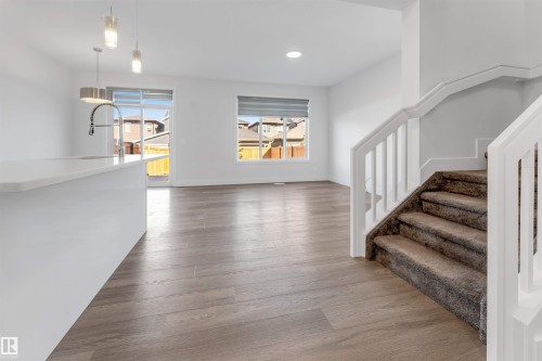 Bright open concept living space featuring light wood-look flooring, white walls, and a staircase with carpeted treads and white railings - 1663 Cavanagh Boulevard Sw, Edmonton, AB - Indoor