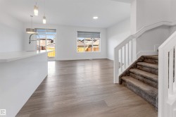 Bright open concept living space featuring light wood-look flooring, white walls, and a staircase with carpeted treads and white railings - 