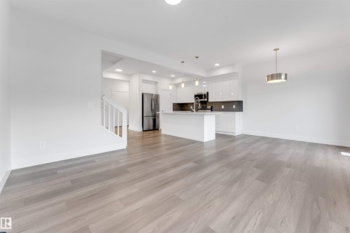Open concept living area with light-toned flooring, featuring a modern kitchen with a central island and stainless steel appliances - 1663 Cavanagh Boulevard Sw, Edmonton, AB - Indoor Photo Showing Kitchen