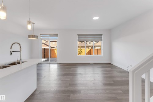 Open concept living space featuring light gray wood flooring, white walls, and a white kitchen island with a stainless steel sink and faucet - 1663 Cavanagh Boulevard Sw, Edmonton, AB - Indoor Photo Showing Other Room
