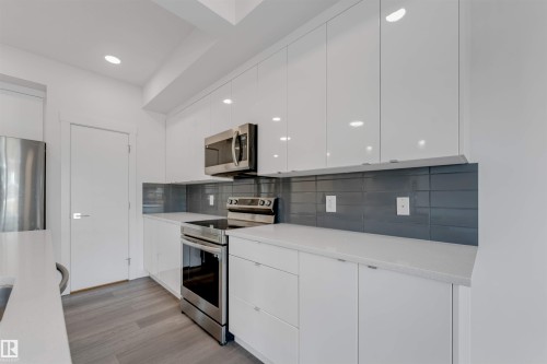 The kitchen features white cabinetry, stainless steel appliances, a dark grey tiled backsplash, and light countertops - 1663 Cavanagh Boulevard Sw, Edmonton, AB - Indoor Photo Showing Kitchen