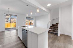 Open concept living area featuring light wood flooring, a kitchen island with a sink and stainless steel dishwasher, and a staircase with carpeted treads - 