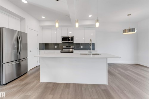 Modern kitchen featuring a white island with a sink, white cabinetry, stainless steel appliances, and a gray tiled backsplash - 1663 Cavanagh Boulevard Sw, Edmonton, AB - Indoor Photo Showing Kitchen With Upgraded Kitchen