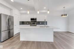Modern kitchen featuring a white island with a sink, white cabinetry, stainless steel appliances, and a gray tiled backsplash - 