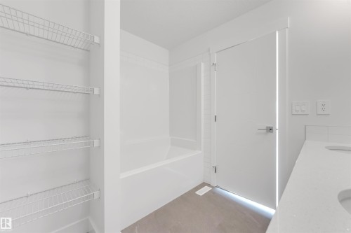 This bathroom features a white bathtub, a vanity with a white countertop and integrated sink, and white wire shelving - 1663 Cavanagh Boulevard Sw, Edmonton, AB - Indoor With Storage