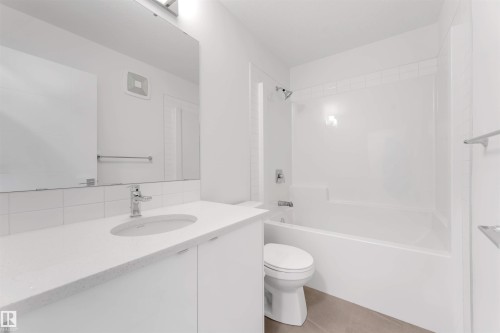 The bathroom features a vanity with a white countertop and an integrated sink, a large mirror, and a bathtub with a shower - 1663 Cavanagh Boulevard Sw, Edmonton, AB - Indoor Photo Showing Bathroom
