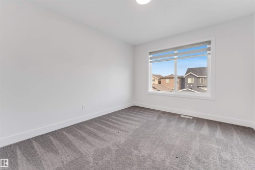 This room features light-colored walls, gray patterned carpeting, and a window with blinds, allowing for natural light - 1663 Cavanagh Boulevard Sw, Edmonton, AB - Indoor Photo Showing Other Room