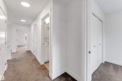 A well-lit corridor featuring neutral-toned carpeting, white walls, and recessed lighting - 