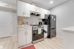 Kitchen featuring light-toned flooring, white cabinetry with silver hardware, a stainless steel range, and a black refrigerator - 