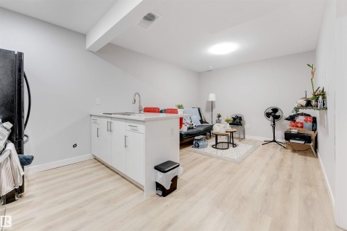 This open-concept living area features light-toned flooring, a bright recessed ceiling light, and a kitchen island with a sink and white cabinetry - 1663 Cavanagh Boulevard Sw, Edmonton, AB - Indoor Photo Showing Other Room