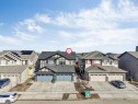 The property features an exterior with light-colored siding and dark trim, a dark-colored roof, and an attached double garage with light blue doors - 1663 Cavanagh Boulevard Sw, Edmonton, AB  - Outdoor With Facade 
