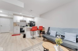 This open-concept living area features light-toned flooring, a kitchen with white cabinetry and stainless steel appliances, and a breakfast bar with seating - 