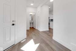 The entryway features light wood-style flooring, white walls, and a white paneled door with black and silver hardware - 