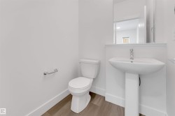 A clean, modern bathroom with a white pedestal sink, toilet, and light wood-style flooring - 