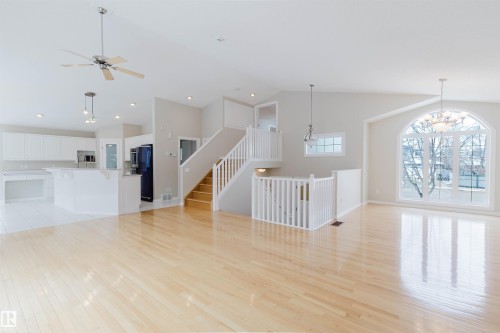 Expansive living space featuring light hardwood flooring, a large arched window, and a grand staircase with white railings - 1641 Forbes Way, Edmonton, AB - Indoor