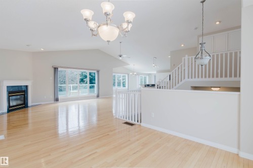 Spacious interior with light hardwood floors, a fireplace with a dark surround, and large windows providing natural light - 1641 Forbes Way, Edmonton, AB - Indoor With Fireplace