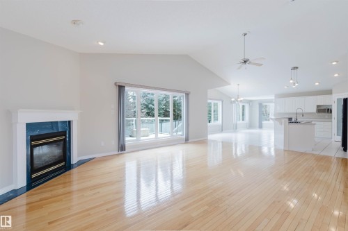 Expansive open concept living area featuring hardwood floors, a fireplace with a blue tile surround, large windows, and vaulted ceilings - 1641 Forbes Way, Edmonton, AB - Indoor Photo Showing Living Room With Fireplace